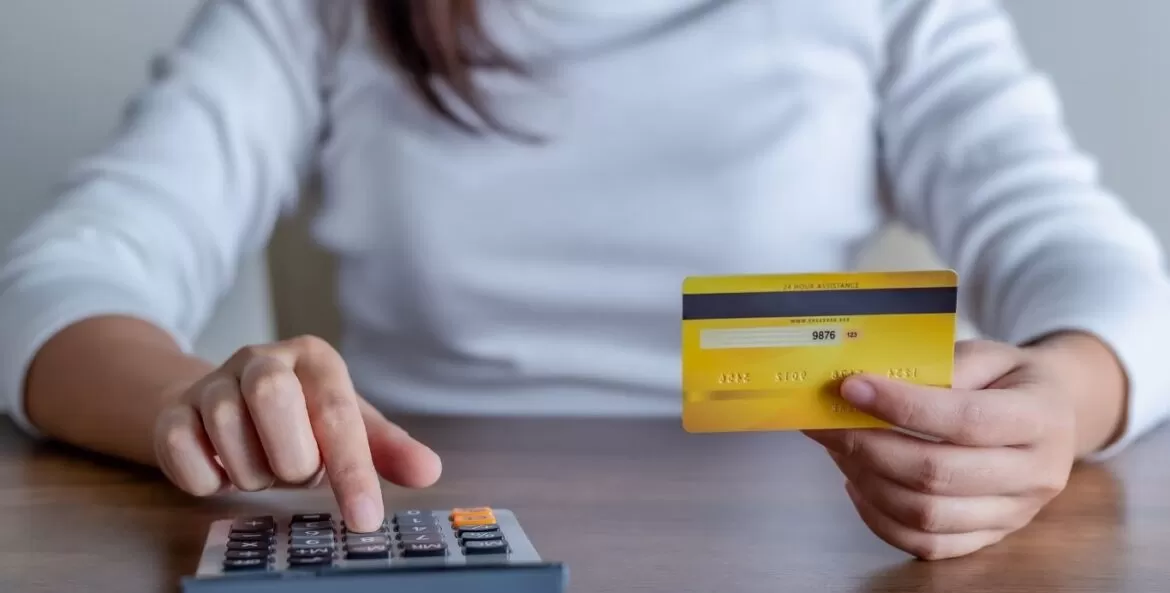 Quanto custa um guarda móveis: mulher segurando um cartão em quanto digita algo na calculadora.