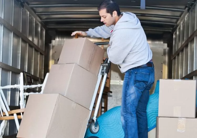 Homem com carrinho de carga carregando caixas que estão dentro de caminhão.