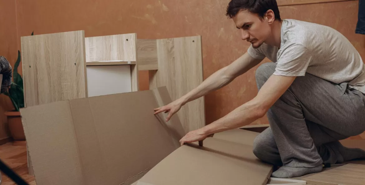como guardar móveis desmontados para não empenar: homem mexendo em caixa de papelão e com vários moveis de madeira desmontados ao redor.