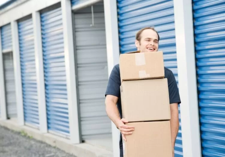 Guarda estoque para empresas: Homem carregando caixas e atrás dele unidades de amarzenamento e uma com a porta aberta.