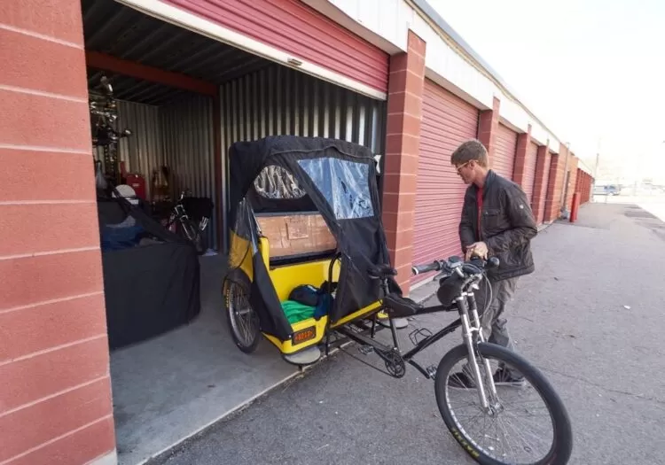 Homem retirando bicicleta com carrinho acoplado de unidade de armazenamento.