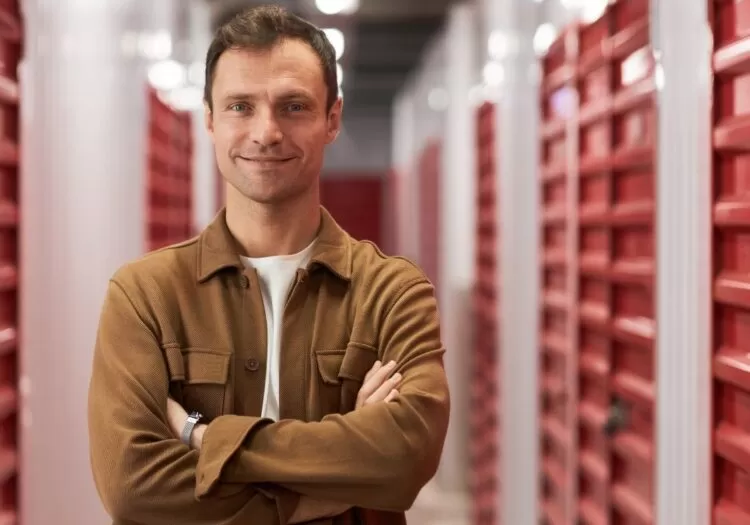 Homem de braços cruzados parado em corredor de self storage