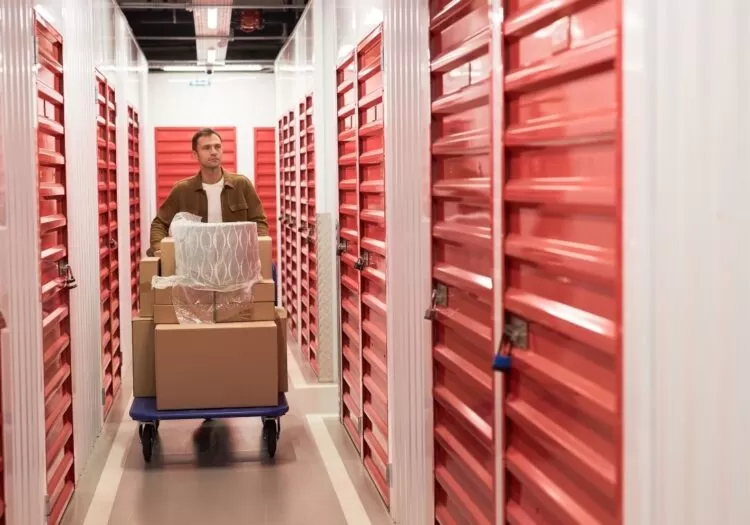 Guarda móveis perto de mim: homem empurrando carrinho com caixas por corredor de guarda móveis