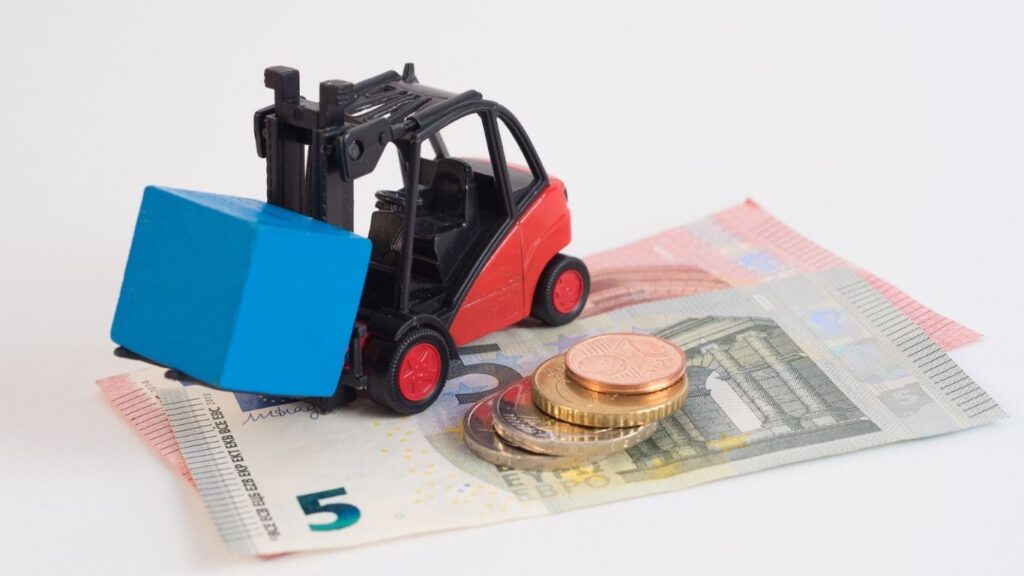 carrinho carregando caixa encima de notas de dinheiro e moedas ao lado