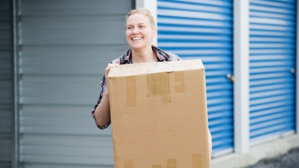 Mulher carregando caixa saindo se unidade de armazenamento.