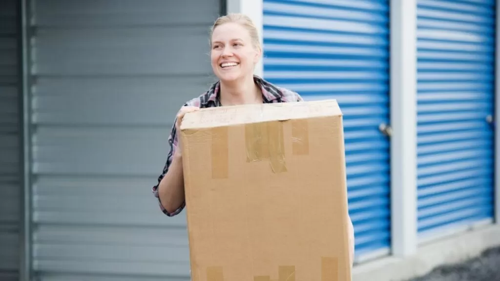 Mulher carregando caixa saindo se unidade de armazenamento.