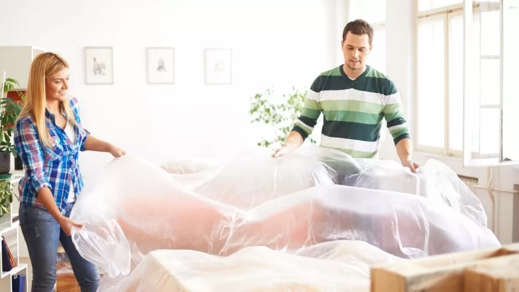 Casal cobrindo móveis com plástico para proteger de poeira.